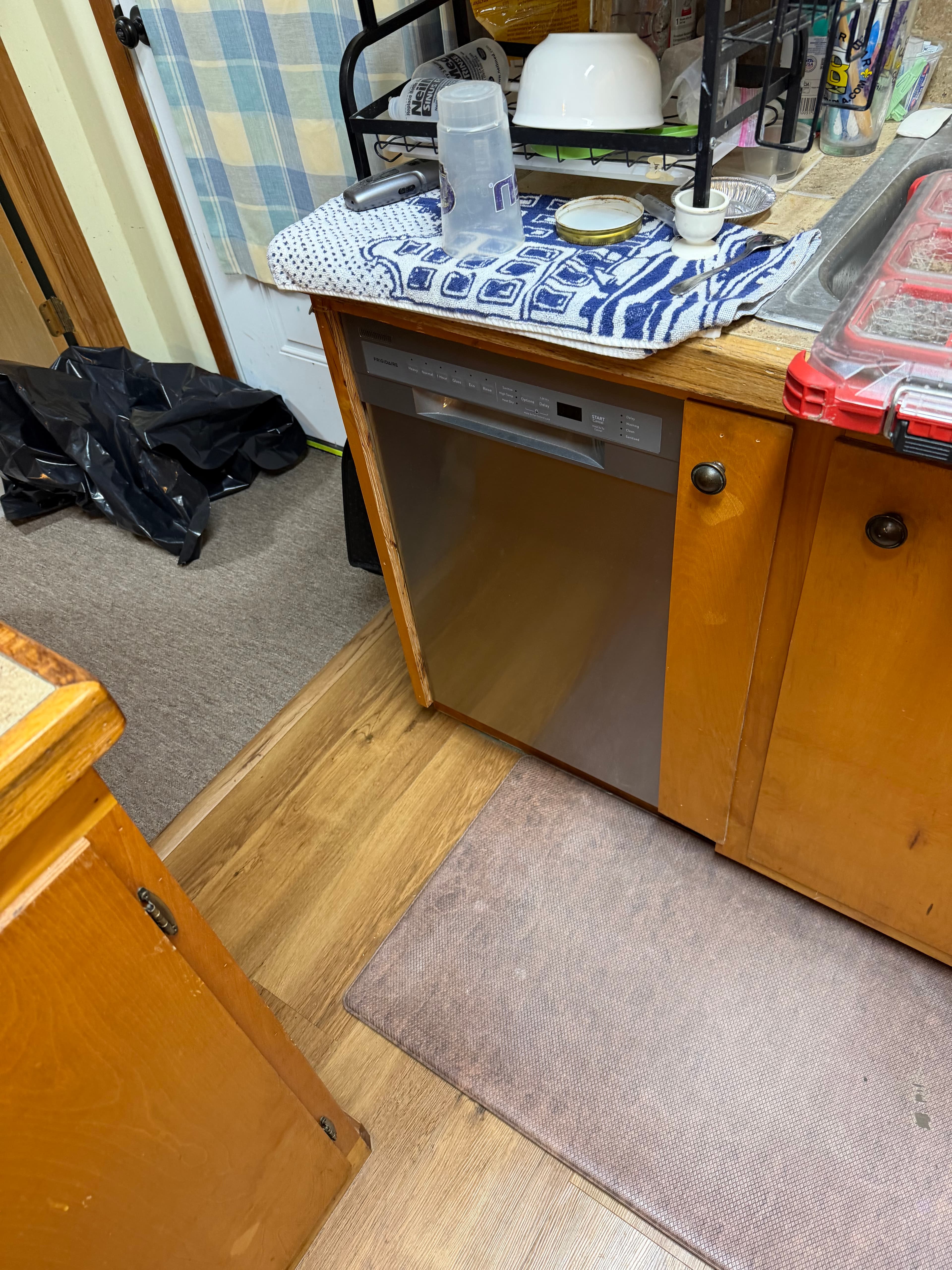 Stainless steel dishwasher in wooden cabinets with a blue patterned towel and dishes on top.