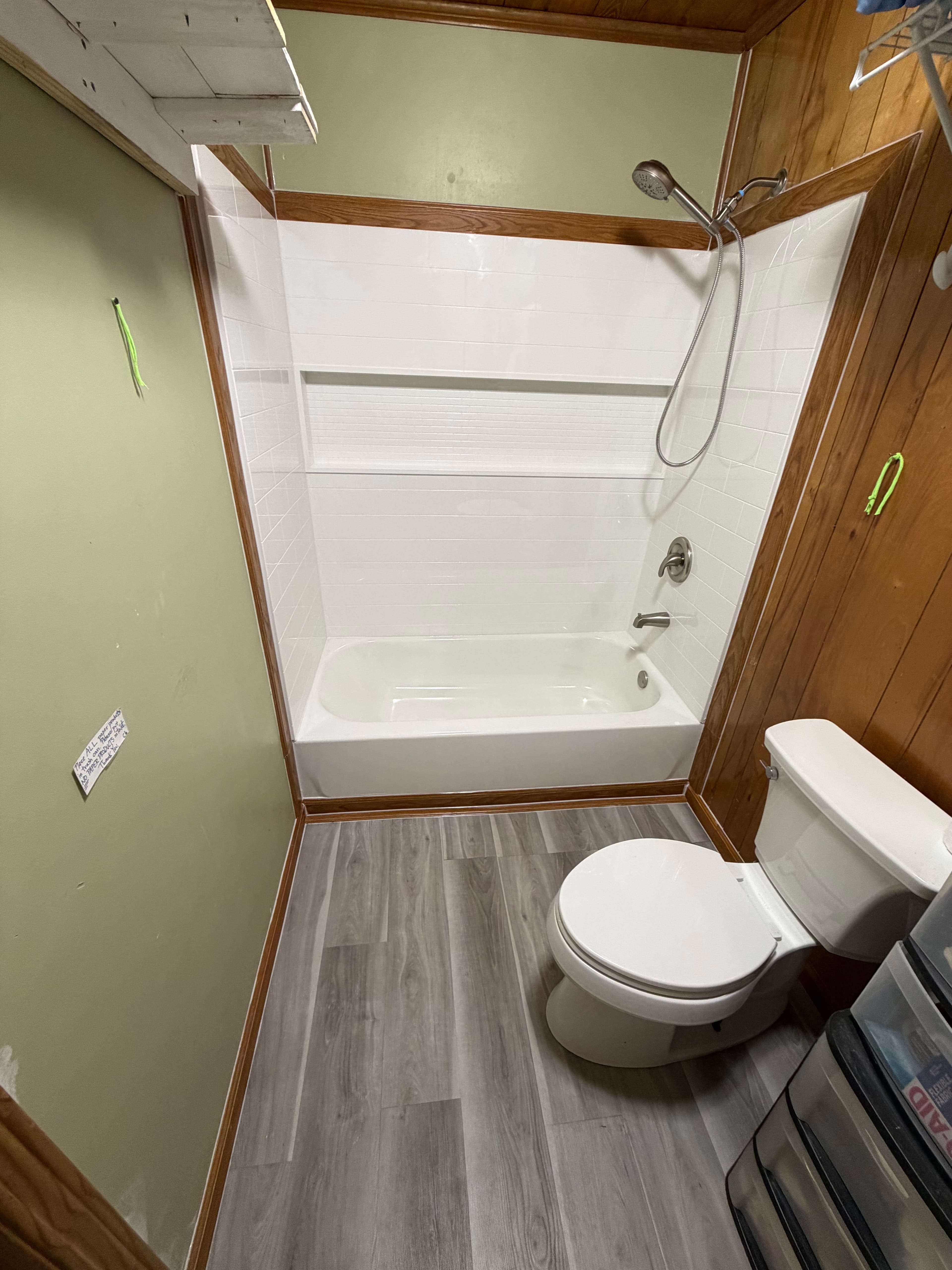 Small bathroom featuring a white bathtub, subway tile surround, toilet, and grey wood-look flooring.
